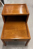 Close-up of single cherrywood step table showing wood grain, drawer with round metal knob, and raised edge top tier.