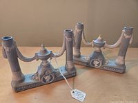 Photo of two gray ceramic or plaster Japanese Regency style taper candlesticks with classical motifs, dual holders on fluted columns and cameos in central pedestals.