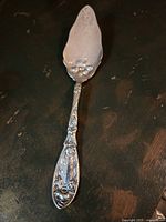 Top-down view of silver plated pie lifter showing detailed floral and vine Art Nouveau design on handle and blade.