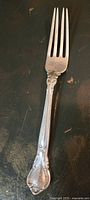 Photo of a Birks sterling silver fork with ornate handle and crooked tines on a dark surface.