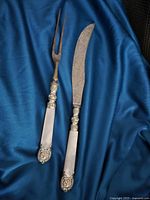 Two-piece carving set with mother-of-pearl handles and ornate sterling silver detail on a blue fabric background.