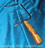 Photo of a metal cheese slicer with a varnished brown wooden handle on a blue fabric background.