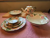 Assorted pieces including plates, cups, saucers, serving bowl and teapot arranged on tabletop.