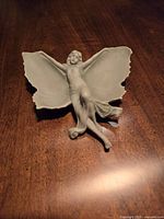 Grey bisque Angel candy dish with detailed facial expression and butterfly-like wings, placed on wooden surface