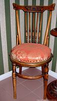 Front view of a maple spindleback chair with a carved crest rail, five turned spindles, and a round upholstered red floral cushion seating.