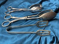 Three mixed silver plated tongs arranged on fabric showing size and style difference.