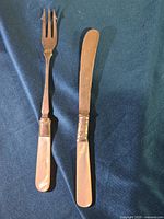 Fruit fork and fruit knife placed side by side on a blue fabric background, showing mother-of-pearl handles and metal parts.