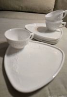 Set of 3 milk glass cups stacked alongside 3 matching triangular sandwich plates, showing embossed floral design and smooth glossy finish.