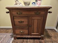 Front view of solid oak washstand showing three drawers and cupboard door with original brass hardware and side turned wood handles.