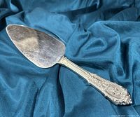 Single pie lifter lying flat on blue fabric background showing detailed Rosepoint silver handle and used stainless steel blade.
