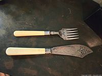 Full view of Victorian pierced blade fish serving knife and fork set with ivory handles on dark surface