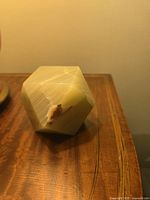 Pale green translucent jade octahedron paperweight with visible natural striations and minor chip on one facet, placed on a wooden surface.