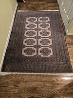 Full view of vintage Bokhara prayer rug laid flat on hardwood floor, showing mocha and brown geometric medallion pattern and multiple borders.