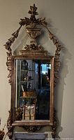 Front view of ornate gold leaf wood wall mirror with carved floral ornamentation and finial