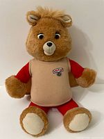 Full view of 1992 Teddy Ruxpin plush with beige vest and red sleeves, sitting upright on white background.
