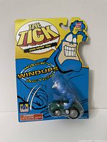 Front view of sealed The Tick Hard Drivin' Tick wind-up toy in yellow packaging with character graphics and Bandai logo.