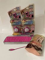 Photo showing two sealed Bratz webcams, two sealed pink Bratz speakers, a pink and silver Bratz keyboard, and a sealed blonde hair extension.