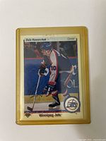Front view of Dale Hawerchuk autographed hockey card in yellow protective plastic casing, showing player in Winnipeg Jets uniform.