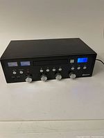 Front view of the black stereo system showing CD slot, control knobs, button panel, and digital display