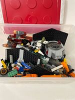 Top view of red Lego box filled with assorted Lego pieces and parts of assembled ships.