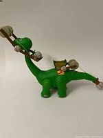 Side view of green Apatosaurus dinosaur toy with a wooden crane arm catapult holding large and small gray rocks secured with yellow elastic bands.