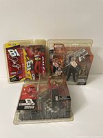 Three sealed NASCAR McFarlane action figures featuring Tony Stewart, Dale Earnhardt Jr., and another driver in original packaging.