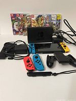 Console in dock with Joy-Con controllers attached, AC adapter and HDMI cable visible, games lined up behind