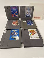 Six Nintendo NES cartridges arranged in two rows with labels facing forward showing game titles Tetris, Top Gun, Double Dribble, 720°, Rollerball, Paperboy.