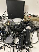 Photo showing multiple PlayStation consoles and controllers tangled with cables and power adapters
