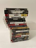 Stack of 18 PS3 game cases showing titles including Tomb Raider, Twisted Metal, Rockband, Ridge Racer, NHL 13, Heavy Rain, Assassin's Creed, Shaun White, GTA, Beatles Rock Band