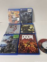 Six PS4 game cases arranged on a flat surface with two Walking Dead 2 discs without case visible to the far right.