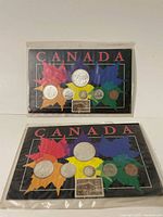 Two 1965 Canadian coin sets on black cards with colorful maple leaf design, each containing six coins and a 5 cent commemorative stamp.