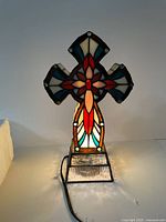 Front view of illuminated cross Tiffany lamp showing red, blue, white stained glass floral pattern and textured glass base.