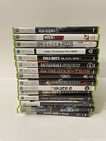 Stack of 15 Xbox 360 game cases showing spines with titles: Dead Rising, NBA 2K8, Street Homecourt, Call of Duty Black Ops 2, Battlefield 3 LE, South Park The Stick of Truth, Red Faction Guerrilla, Ghostbusters, Skate 2, Call of Duty Ghosts, WWE Legends of WrestleMania, Hunter Edition, Genesis, Jurassic Park The Game, and a recycled Call of Duty game.