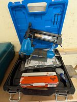 Mastercraft air driven brad nailer in blue and black color within blue hard plastic carrying case. Includes instruction manual and box of Paslode brad nails.