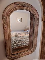 Front view of the antique mirror showing the full arched rectangular glass and the wooden patina frame with floral plaster decorations.
