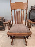 Front view of antique oak rocking chair with upholstered seat and wooden spindles on back and arms.