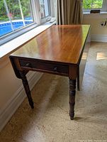 Side view of table with one drop leaf extended, showing turned legs and drawer front.