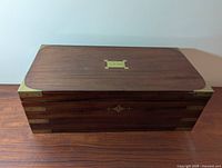 Closed box showing mahogany exterior, brass corner accents and inlaid nameplate reading E.M.Miles