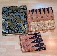 Two folded batik fabric panels placed on a wood floor, showing different traditional patterns and colors.