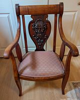 Front view of carved tropical wood armchair highlighting the Bacchus face carving on backrest and cushioned seat.