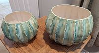 Two ceramic fluted planters side by side on a wooden floor showing their shape and glaze finish.