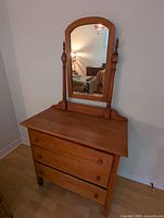 Front view of the cherry wood dresser showing three drawers and attached tilting mirror.