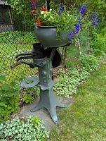 Full view of antique cream separator with planter viewed at an angle, showing metal basin filled with colorful flowers and detailed hand crank.