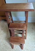 Front view of solid cherry folding kitchen stool showing top surface, steps and frame.
