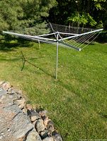 Four-sided metal folding clothesline fully extended in outdoor grassy area.