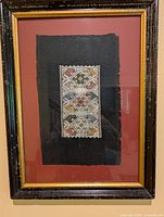 Framed textile showing the full tapestry artwork centered on black fabric and surrounded by red matte and dark wooden frame.