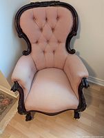 Front view of antique gentleman's chair showing tufted pink upholstery and carved wooden frame