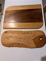 Two wooden cheese boards shown together, oak and walnut board on top, cherry wood board with live edge below.