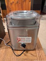 Front view of the stainless steel Cuisinart ice cream maker with control knob and power cord visible.